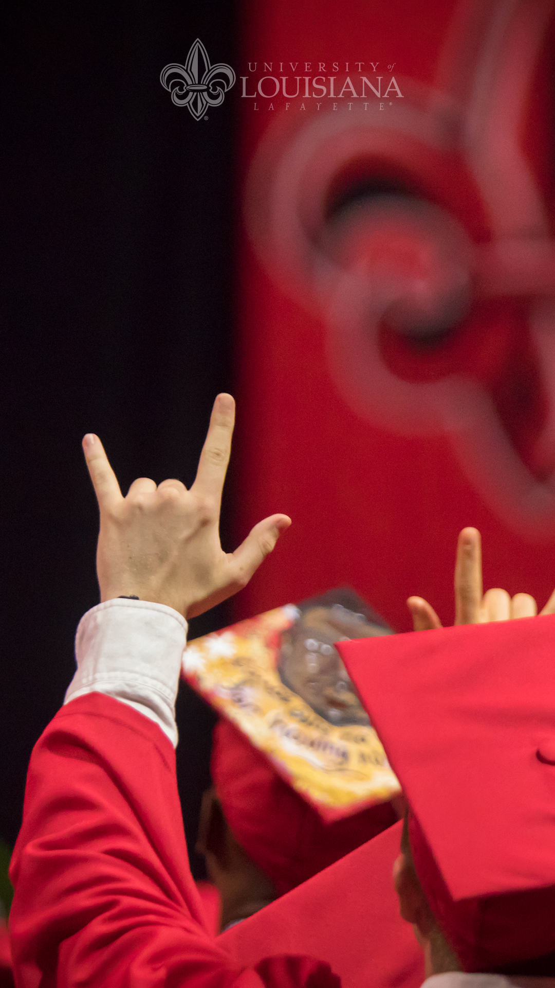 Photo of a caucasian UL Lafayette graduate from behind with his hand raised in the UL hand sign.